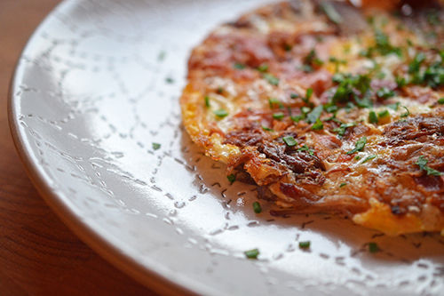 A side view of Pig in a Skillet topped with minced herbs on a white plate.