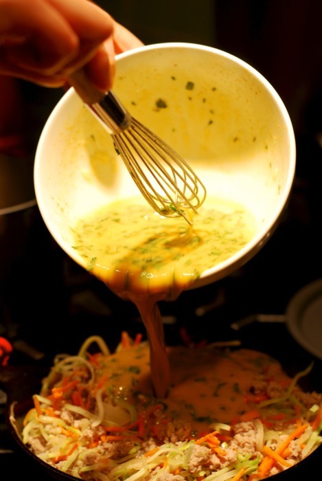 Someone pouring in an egg mixture into a cast iron skillet for the paleo and whole30 recipe of curried ground pork and broccoli slaw frittata.
